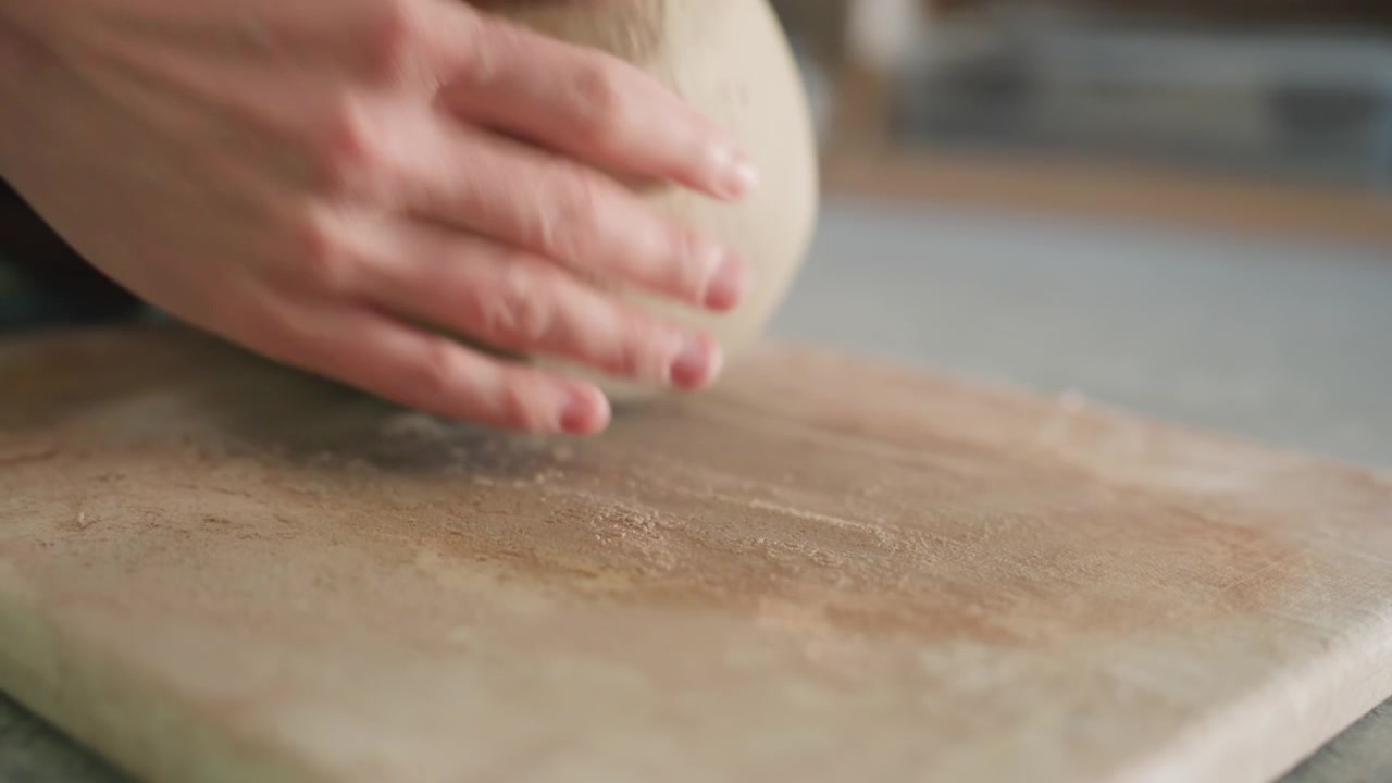 Pezzo di argilla sul piano di lavoro, vasaio che impasta e modella l'argilla con mani ferme, residui sabbiosi sul piano, texture morbida e terrosa. Primo piano del processo tattile in un laboratorio di ceramica, artigiano concentrato.