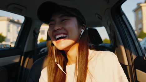 happy young woman laughing while using phone and earphones in car