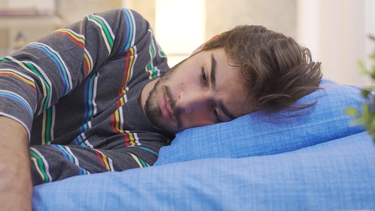 Young man with anxiety disorder lying thoughtfully in his bed.