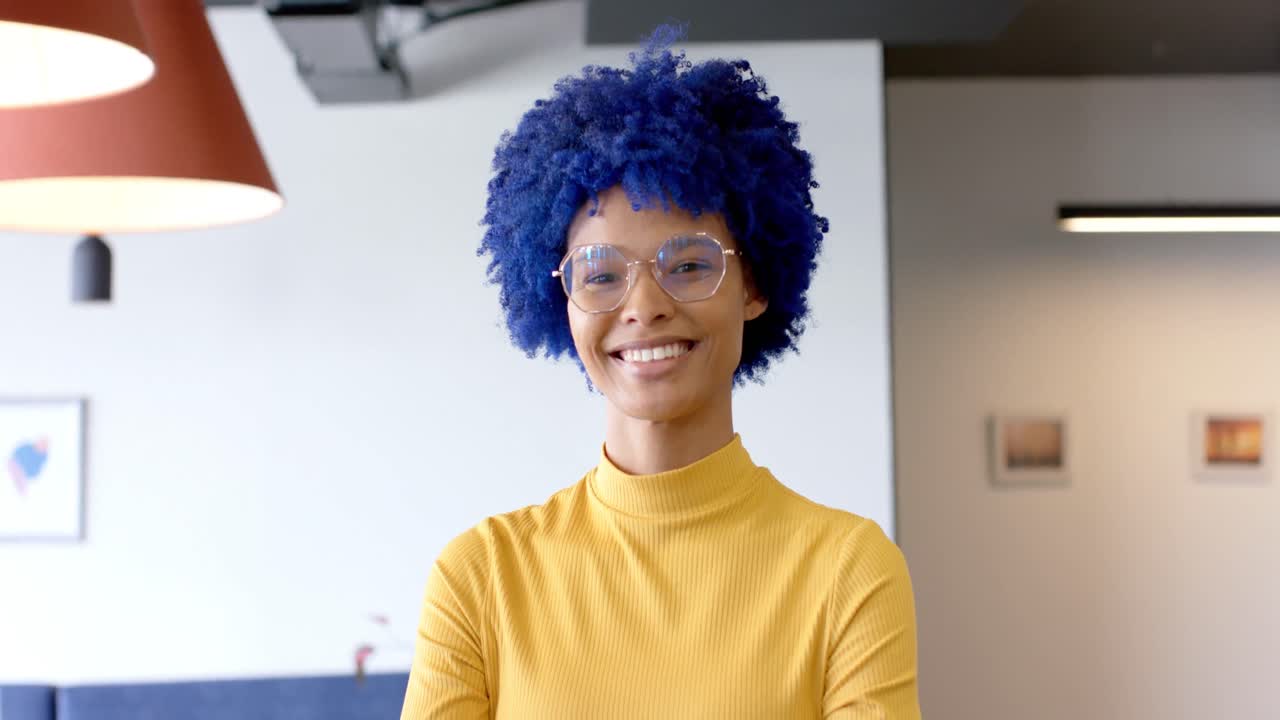 retrato de una feliz mujer de negocios creativa biracial con afro azul sonriendo en la oficina, en cámara lenta