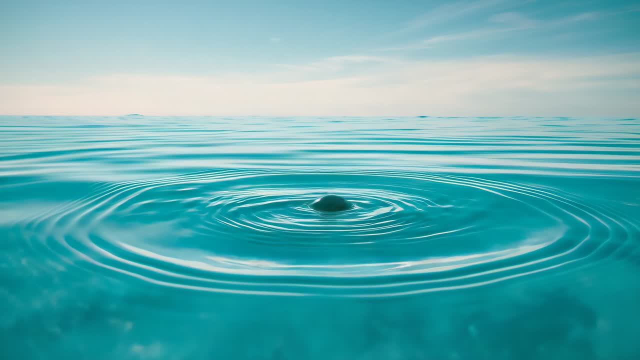 Droplet puncturing surface as column forming in turquoise sea, creating concentric ripples outward