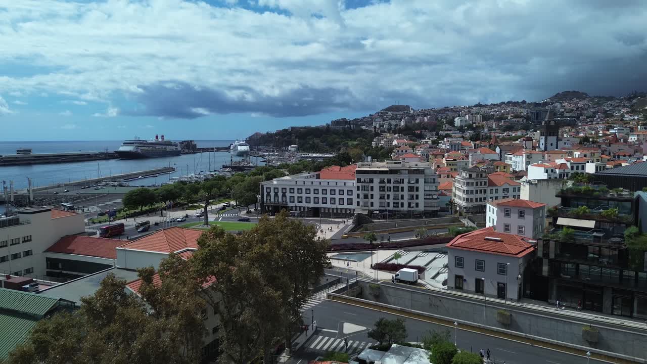 Airplane window view over Funchal, Madeira. Dense city rooftops spread across hills. A cruise ship visible on the ocean horizon to the left.