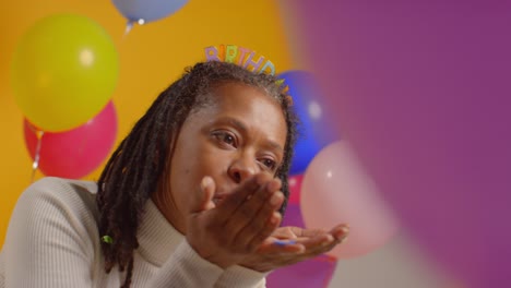 studio portrait of woman wearing birthday headband celebrating blowing paper party confetti