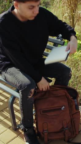 man sitting on a bench in the nature searching for something in the backpack