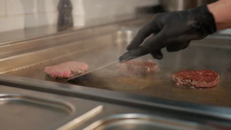 restaurant chef flipping patties with spatula on hot steaming stove, static shot