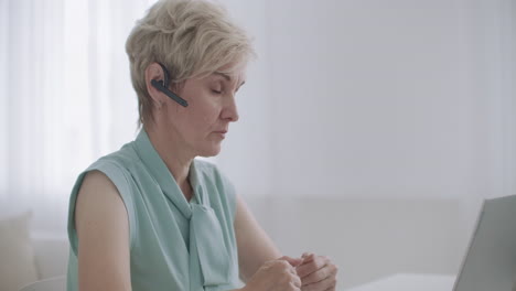 aged lady is communicating online by videocall using headset and notebook online consultation and distant work