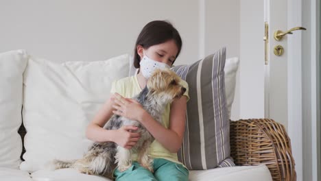 chica con máscara facial sosteniendo a su perro mascota en casa