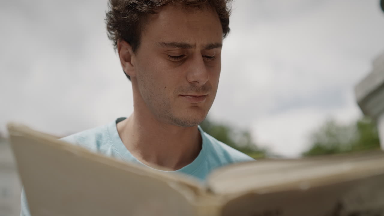 joven sentado en el parque tivoli y leyendo un libro, el sol brilla sobre él en el día de verano