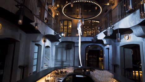 female aerialist doing a front split pose climbing on silks in a club