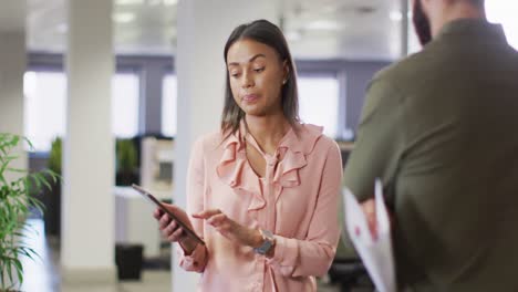 Video-of-diverse-businesswoman-and-businessman-using-tablet-and-talking-in-office