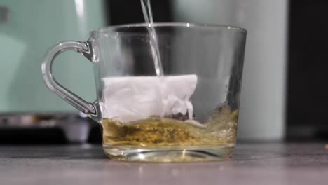 boiling water being poured into a glass mug containing a tea bag