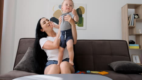 Beautiful-Mom-Sitting-On-Sofa-In-Living-Room-Playing-With-Her-Adorable-Little-Boy-While-Having-A-Video-Call-At-Home