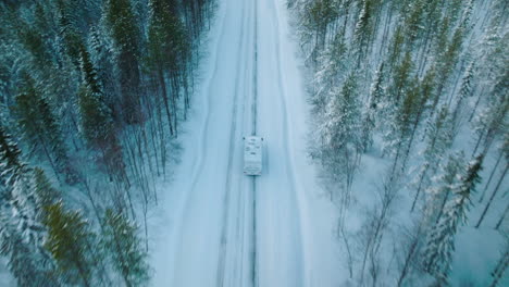 white camper driving on snowy road in lapland finland - aerial shot