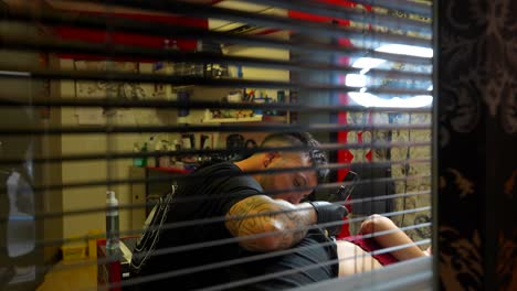 static shot from a window of a tattoo artist tattooing and listening to his female customer