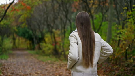 following the lady with beautiful long dark hair walking in the park. woman turns her head smiling to the camera. autumn nature backdrop.