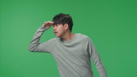 asian man looking at something while standing in front of green screen background