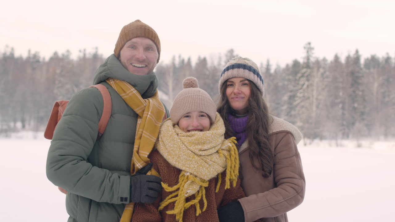 겨울옷을 입은 아버지, 어머니, 딸이 눈 덮인 숲에서 포옹하고 카메라를 바라보는 모습