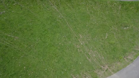 Drohnenluftaufnahme,-Die-Sich-Langsam-Um-Einen-Einzelnen-Radfahrer-Dreht,-Der-Auf-Einer-Von-Gras-Umgebenen-Bergstraße-Radelt