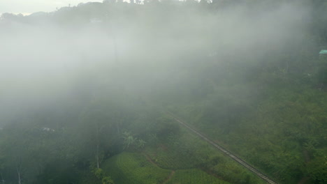 establishing aerial drone shot through the mist of train track in hills around ella sri lanka