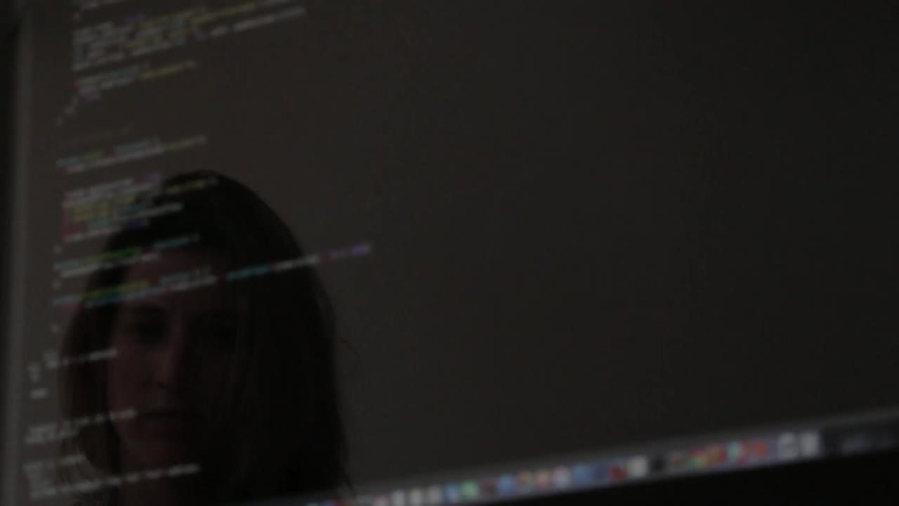 Reflections of a girl coding on a computer are visible on the screen or nearby surface