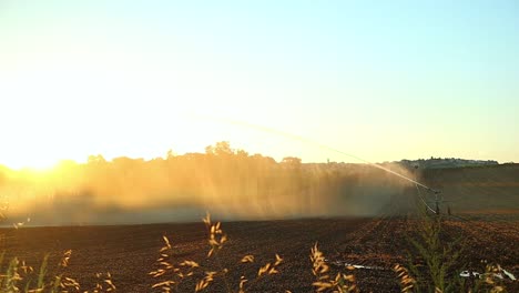 Equipos-De-Riego-Y-Riego-En-Campos-De-Cultivo,-Salpicaduras-De-Agua-Y-Pulverización-Al-Atardecer-En-Suelos-Agrícolas-En-Cingoli,-Italia,-Vistas-Panorámicas