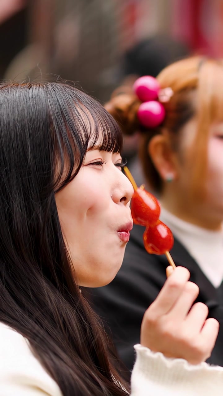 Primo piano di una donna felice che gusta cibo da strada a base di frutta candita a Tokyo, Giappone.