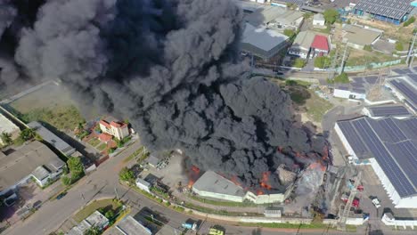 Aerial-shot-over-burning-warehouse-caused-by-explosion,-black-cloud-of-smoke-rising