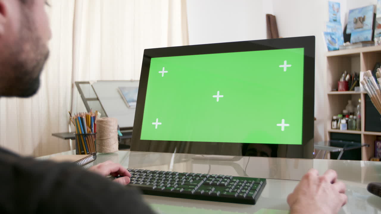 Man using computer with green screen in home office