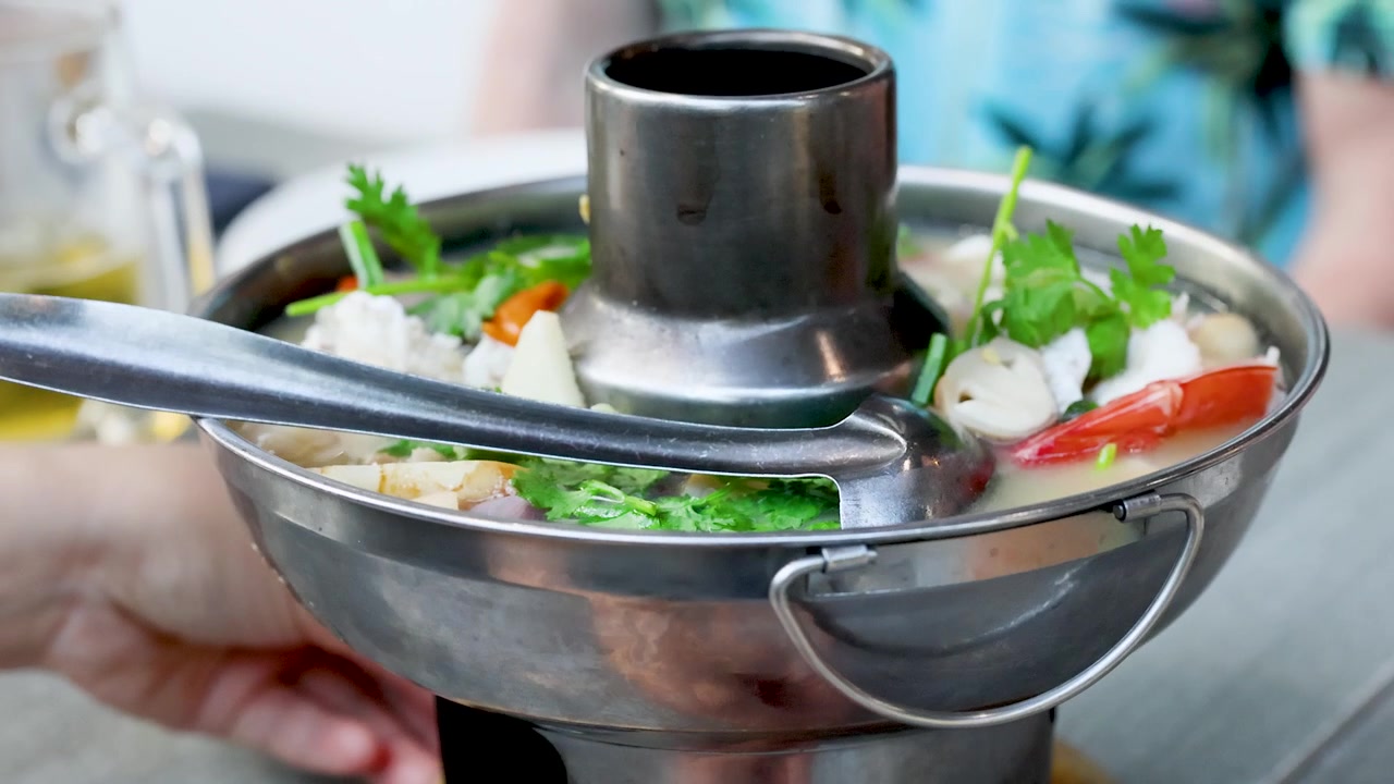 Nærbilde av dampende krydret sjømatssuppe servert i en tradisjonell metallgrytebolle