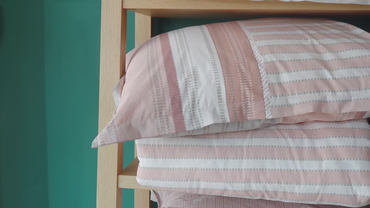 Bantal dan Seprai Bergaris Merah Muda dan Putih di Rak Kayu