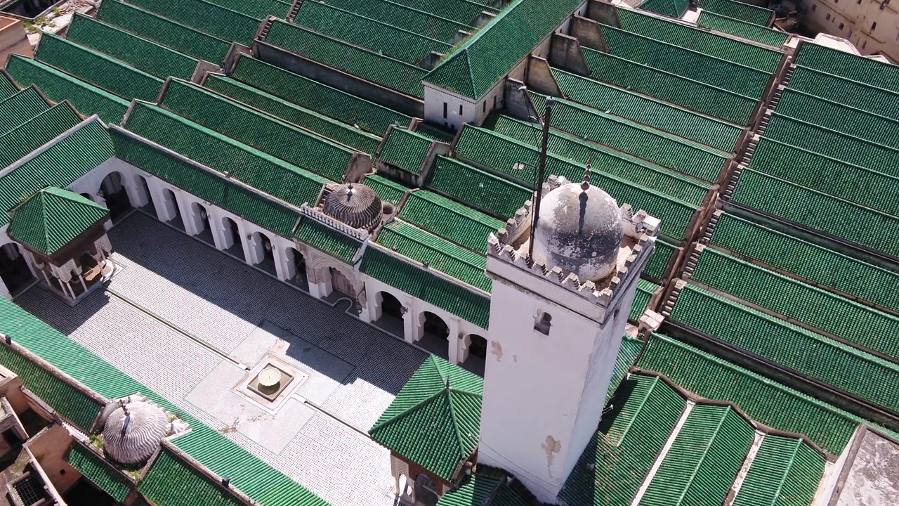 Prospettiva aerea con drone che mostra ampie file di tetti in tegole smaltate verde smeraldo, minareto bianco e cortile tradizionale della Moschea Al Quaraouiyine a Fez, Marocco