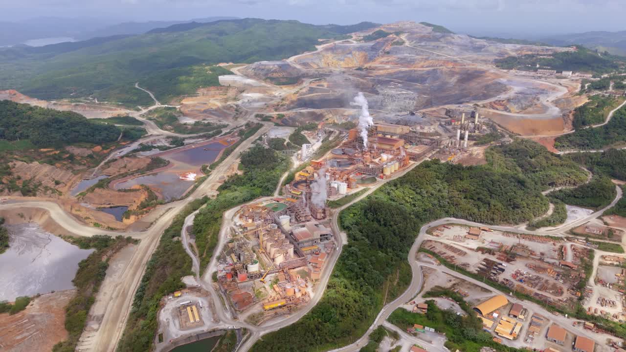Pueblo Viejo mine, a large open-pit gold operation, industrial processing plant with smoke from smokestacks, surrounded by excavated landscape, Barrick Gold, Dominican Republic. Aerial drone