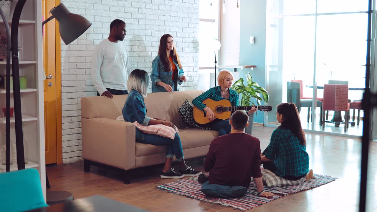 En gruppe venner af forskellige nationaliteter synger sange og spiller guitar i et stort moderne studie.