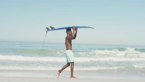 hombre afroamericano sosteniendo una tabla de surf en su cabeza