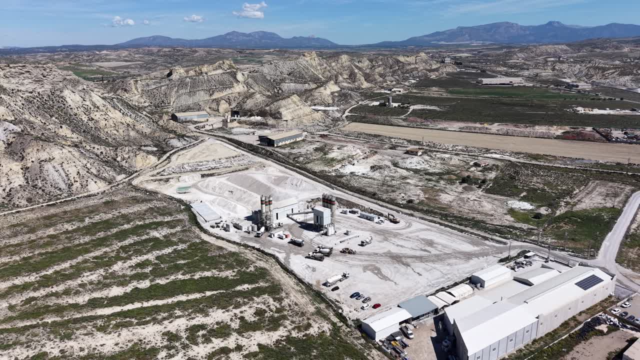 Una ripresa con drone in allontanamento di una fabbrica di cemento e ghiaia vicino a Lorca, che mostra i macchinari pesanti, i silos e le materie prime sotto un sole splendente a Murcia
