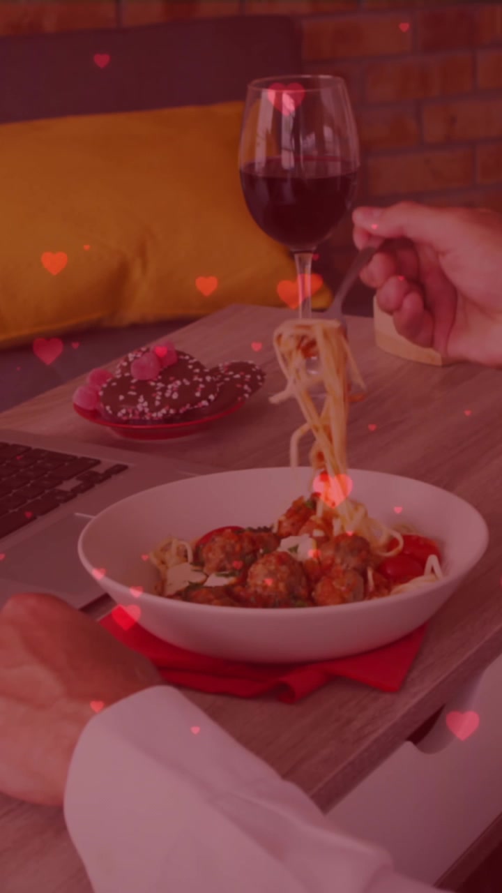 Icone a forma di cuore rosso che fluttuano sopra un uomo caucasico che pranza mentre fa una videochiamata sul laptop