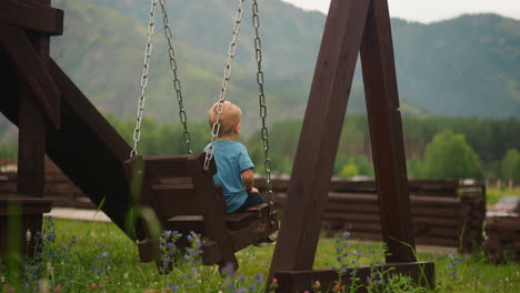 lonely boy sits on swings on playground against mountains