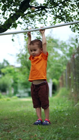 sportive caucasian baby hanging on the horizontal bar outdoors. energetic active male kid exercising in the park. vertical video.