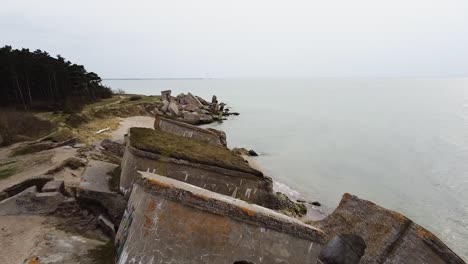 aerial view of abandoned seaside fortification building at karosta northern forts on the beach of baltic sea in liepaja in overcast spring day, wide establishing drone ascending shot moving forward