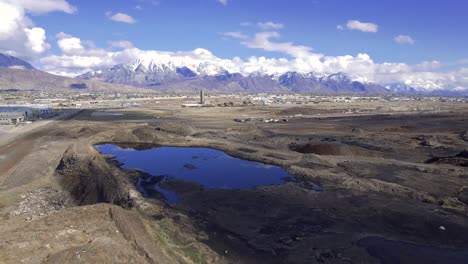 The-snow-capped-Wasatch-Mountains-and-Mount-Timpanogos-rise-above-Utah-County-as-a-drone-flies-over-the-catch-pond-and-slag-heaps-leftover-from-the-Geneva-Steel-Mill-plant