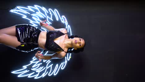 glamour ethnic woman dancing in studio against neon wings