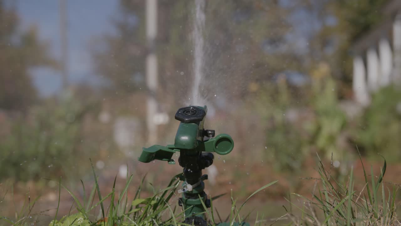 Filmato in slow motion di un irrigatore che annaffia il prato con lo sfondo sfocato