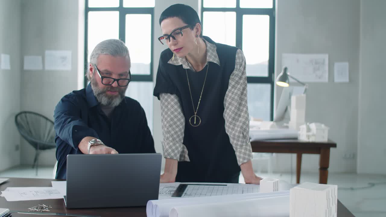 dos colegas discutiendo un proyecto en una computadora portátil en una oficina de arquitectura