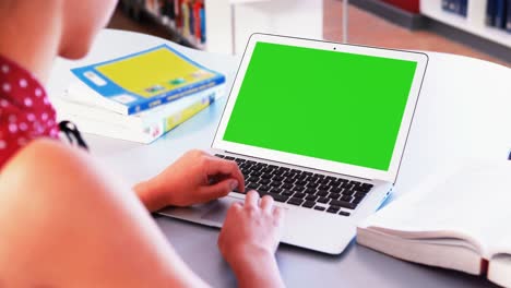 niña de escuela usando una computadora portátil en la biblioteca