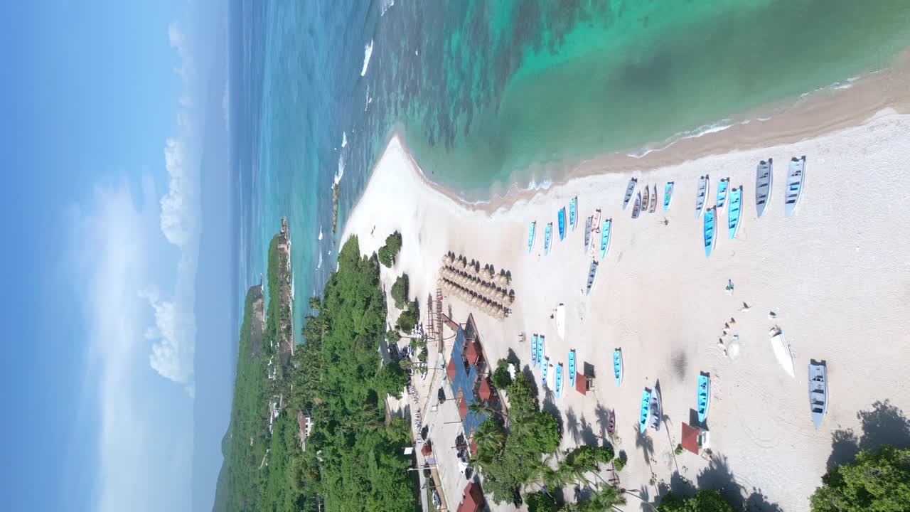 Vertical aerial shot over sandy beach with boats and sunshades during beautiful sunny day on Caribbean island