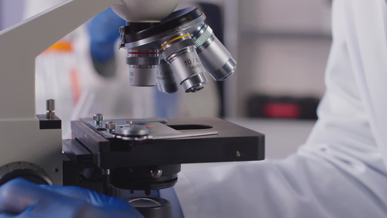 Close Up Of Female Lab Worker Or Phlebotomist Analysing Blood Samples In Laboratory With Microscope