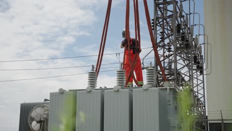 una construcción de trabajo está atando las cuerdas que cuelgan de una grúa en las esquinas de un transformador para que pueda ser llevado