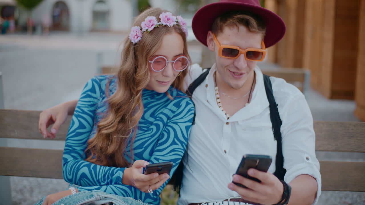 pareja sentada al aire libre en un banco mirando teléfonos