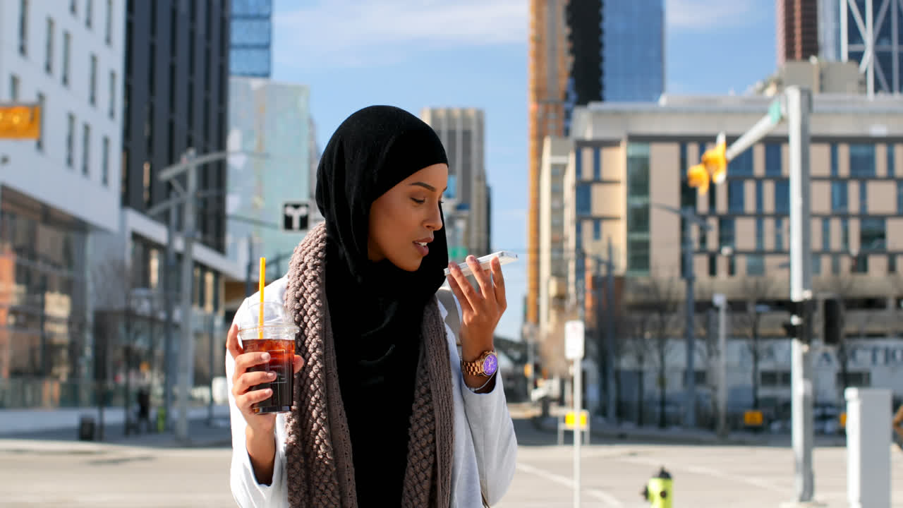 Front view of young Asian woman in hijab talking on mobile phone in the city 4k