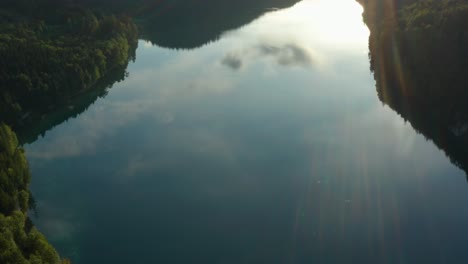 aerial pan up, alpsee reflection of mountains and clouds, lens flare